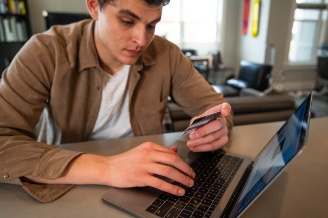 Young man making an online payment with his card and phone at his laptop