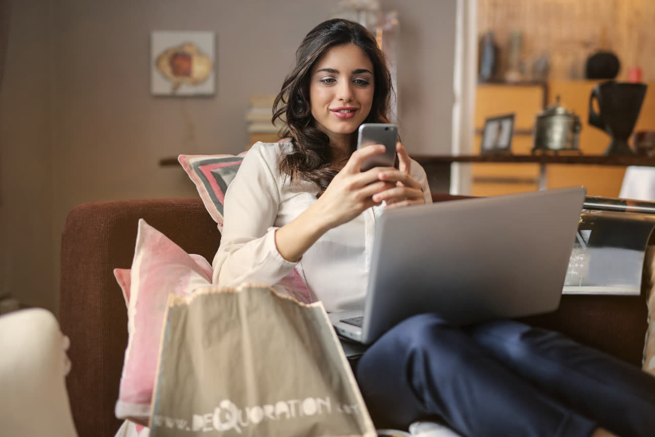 Mujer con bolsas de compras revisa una promoción en su celular desde casa