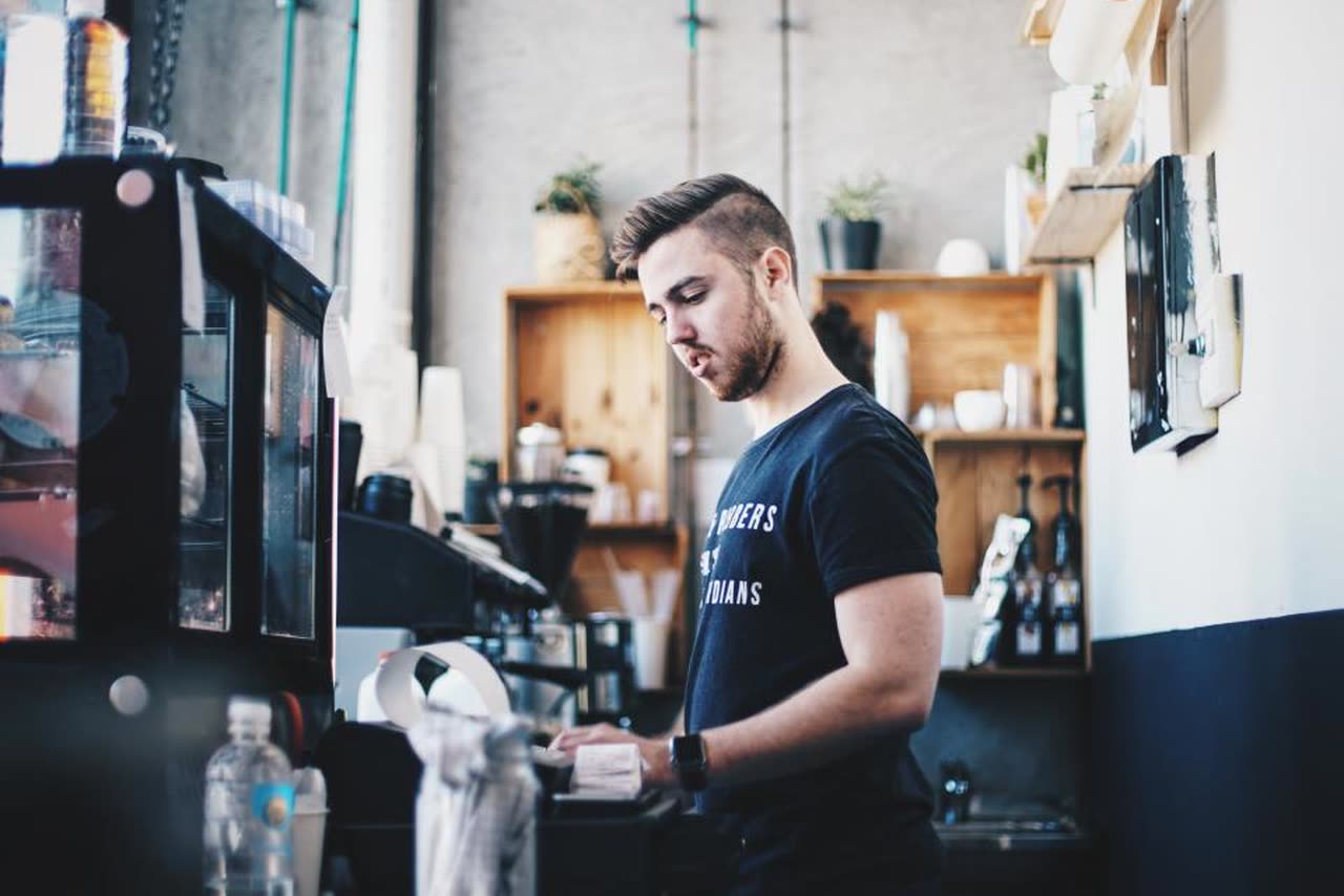 A coffee shop owner prepares an order behind the counter of his business
